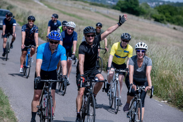 A group of cyclists having fun one with his hand raised up in the air.